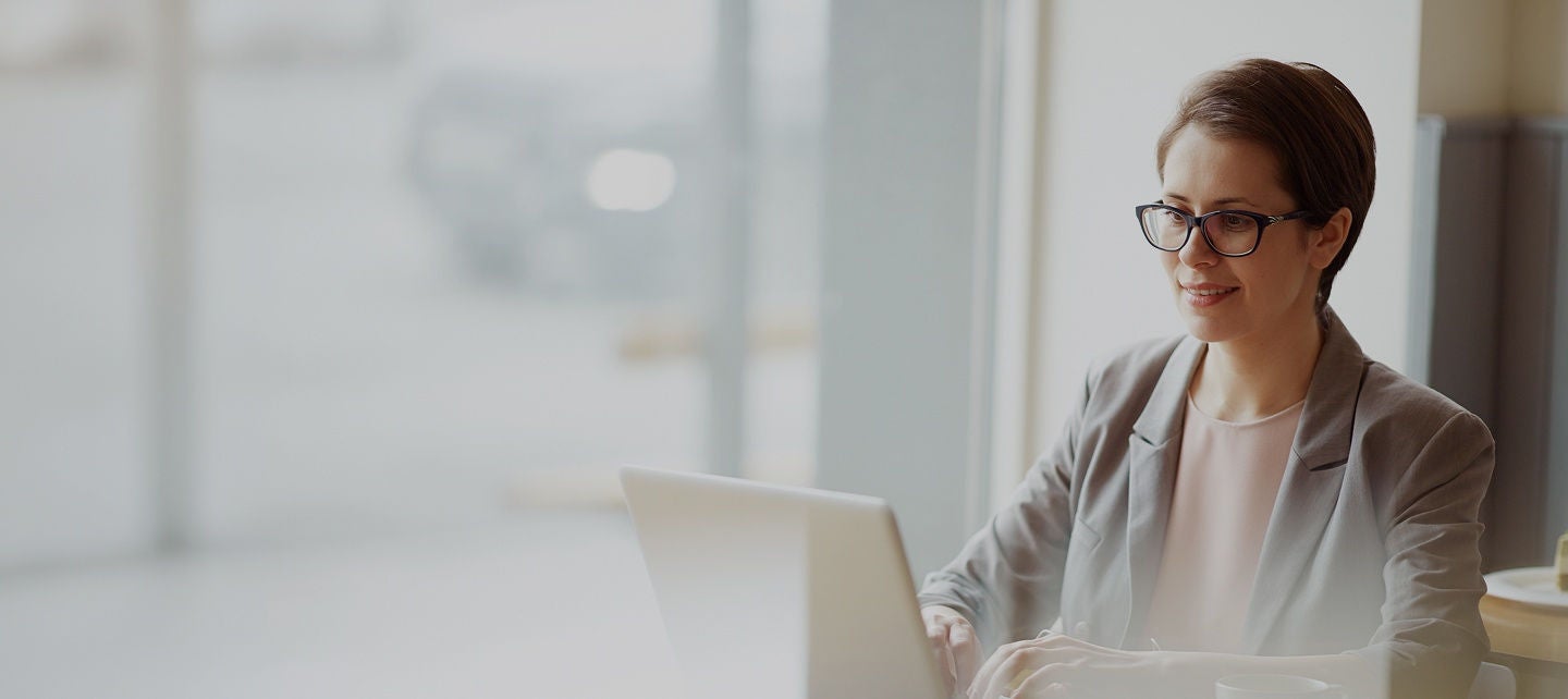 Woman wearing glasses working on a laptop at a desk.