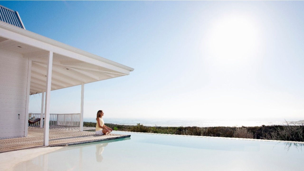 A woman sits in a yoga pose at the edge of an infinity pool.