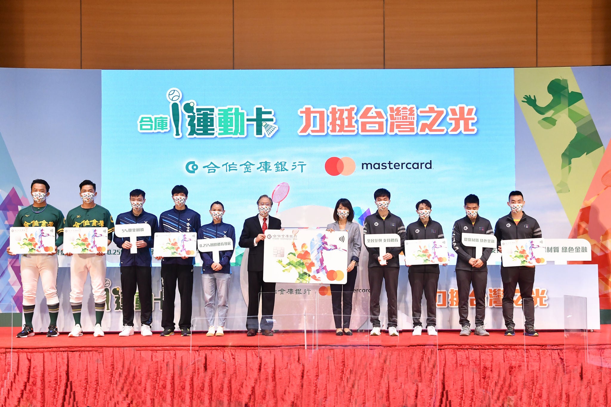 Eleven people in sportswear and business attire stand on a stage holding oversized card cutouts, in front of a backdrop with logos and Chinese text.