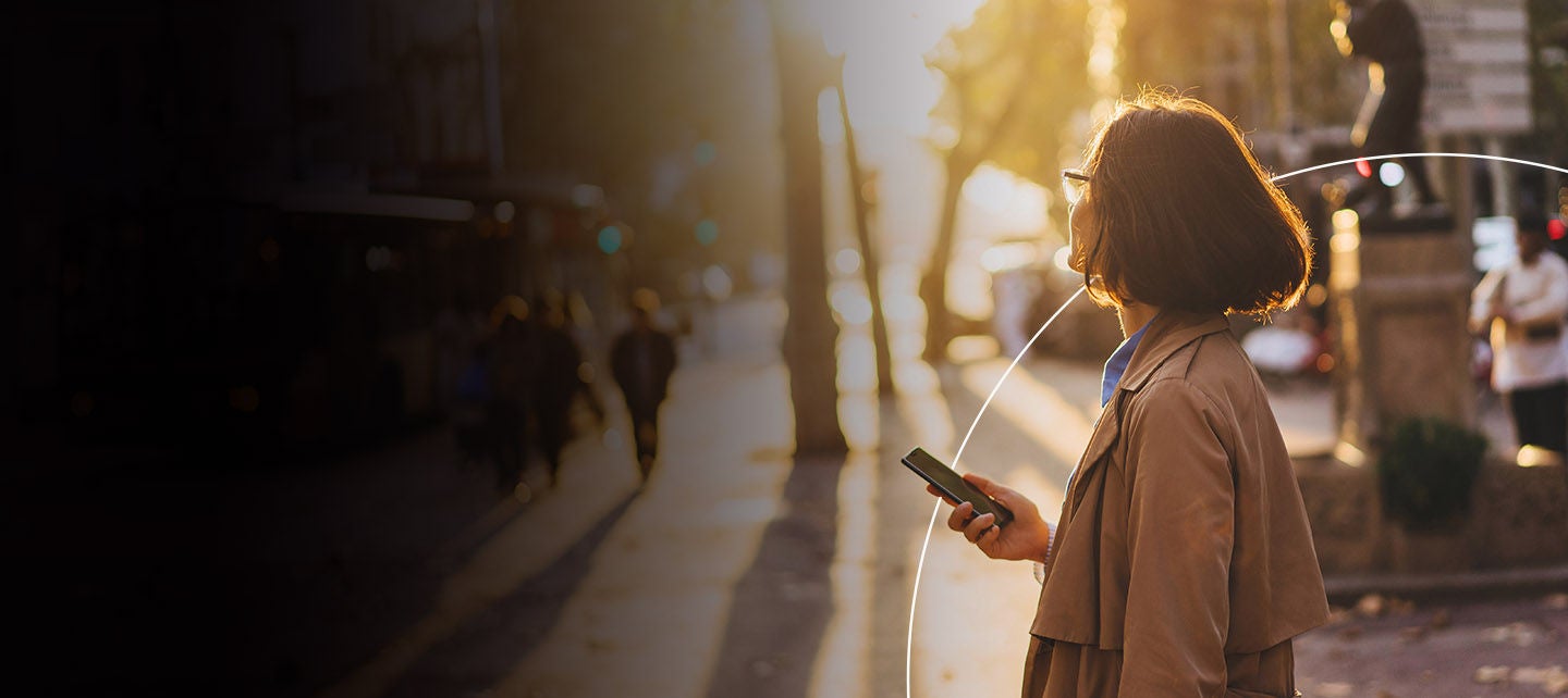 Žena drži mobitel dok šeta parkom. 