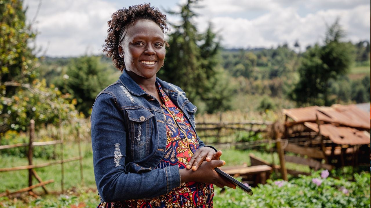 A woman smiles in front of her farm. 