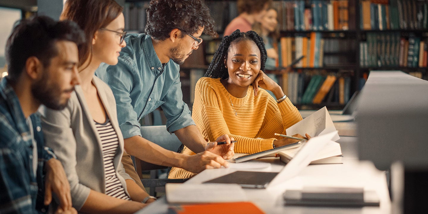 Team collaborating at a desk, with a smiling woman in a yellow sweater at the center.