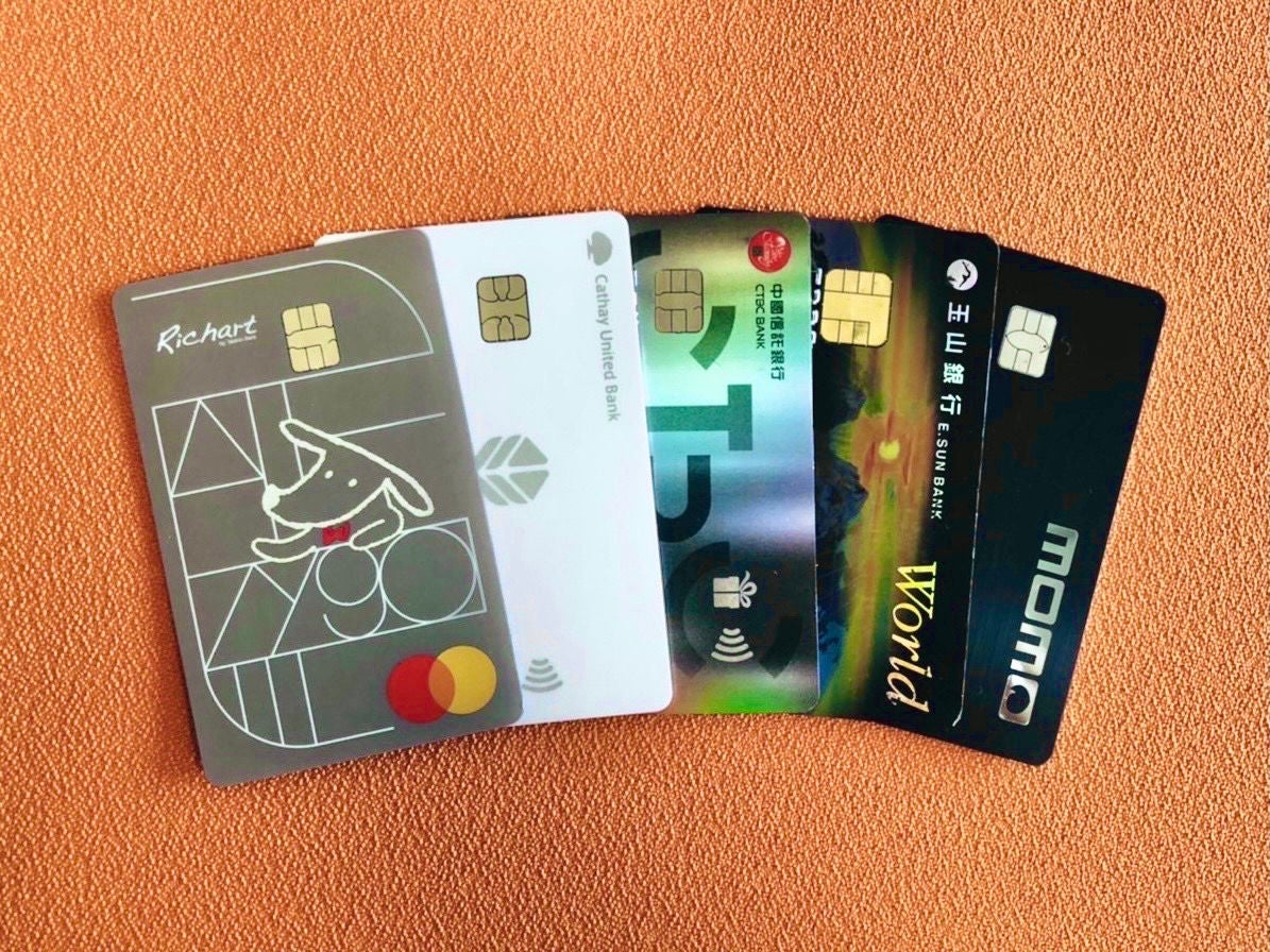 Five payment cards from different banks fanned out on an orange-textured surface.