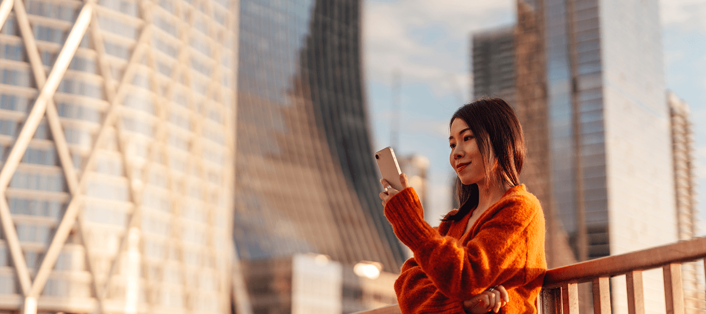 Woman in orange looking at her phone outside