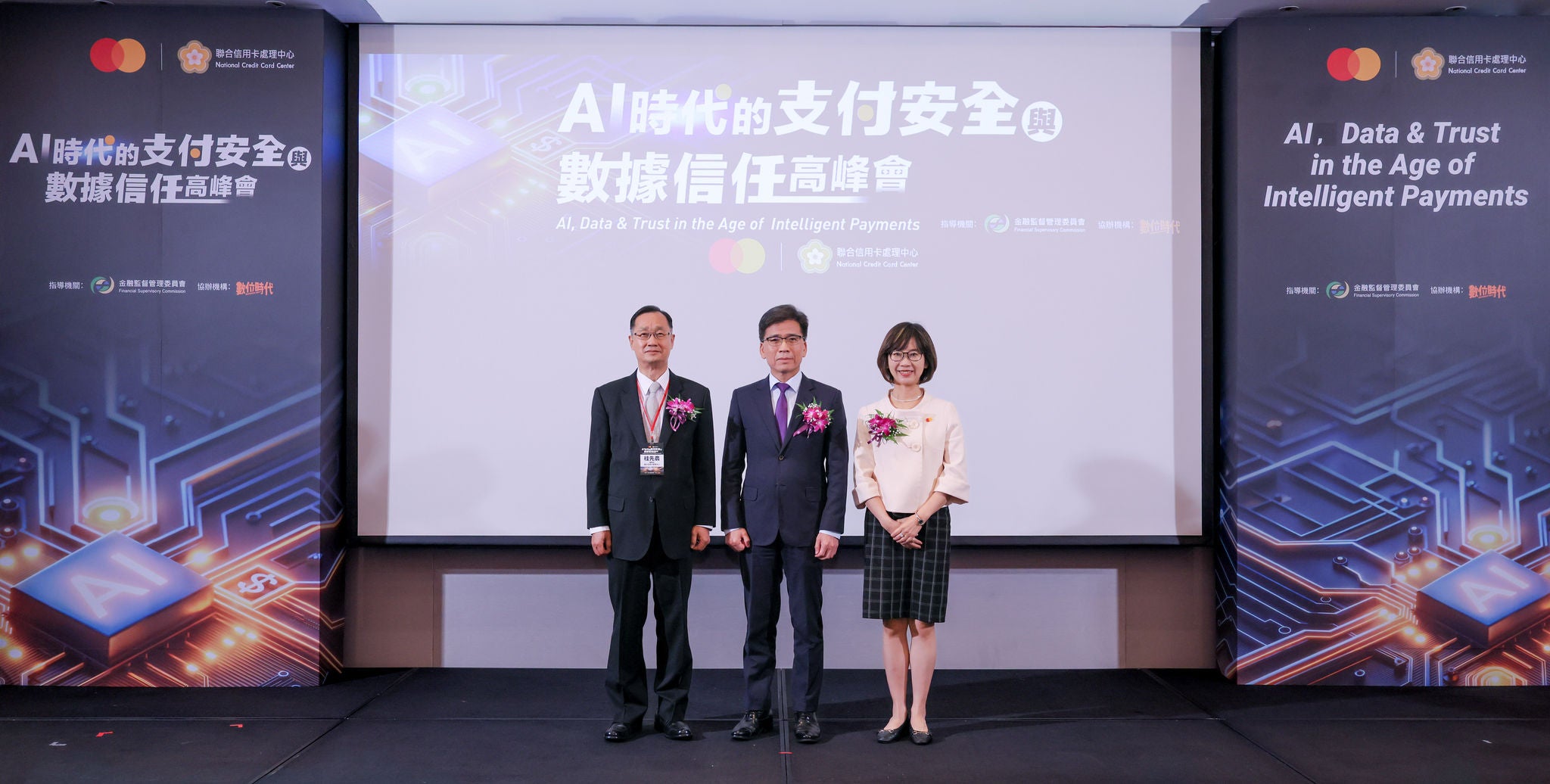 Three people in business attire stand together on a stage in front of a large presentation screen at a conference.
