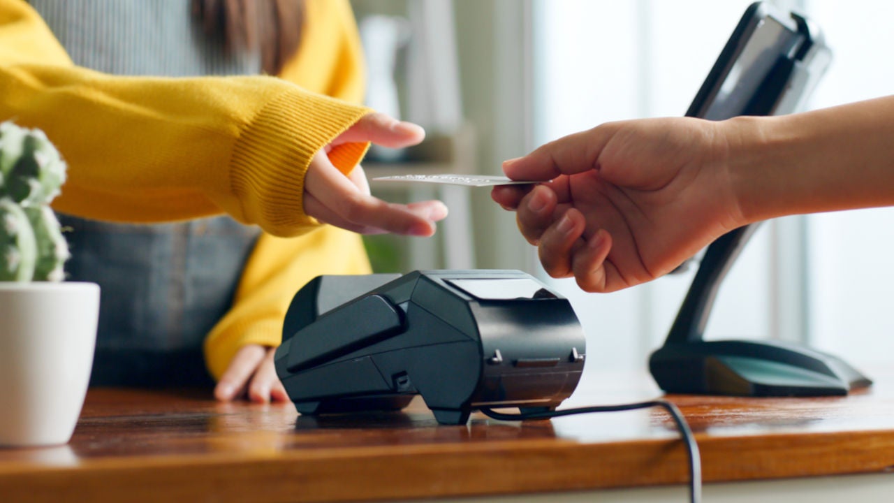 A hand handing a card to a lady in yellow cardigan over a payment terminal.