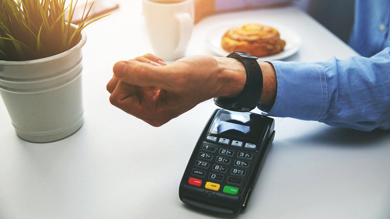 Close up of man's arm paying for danish and coffee by taping watch on terminal