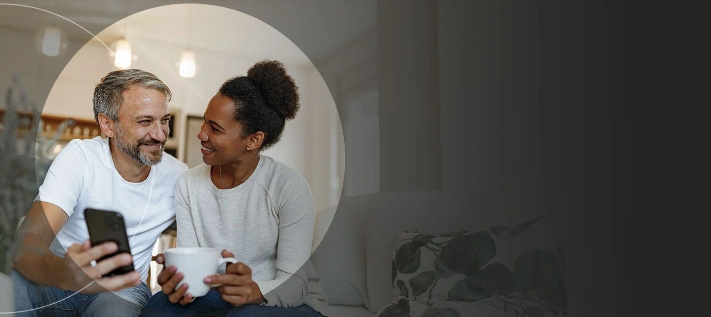 גבר ואישה מביטים במכשיר טלפון ומחייכים.