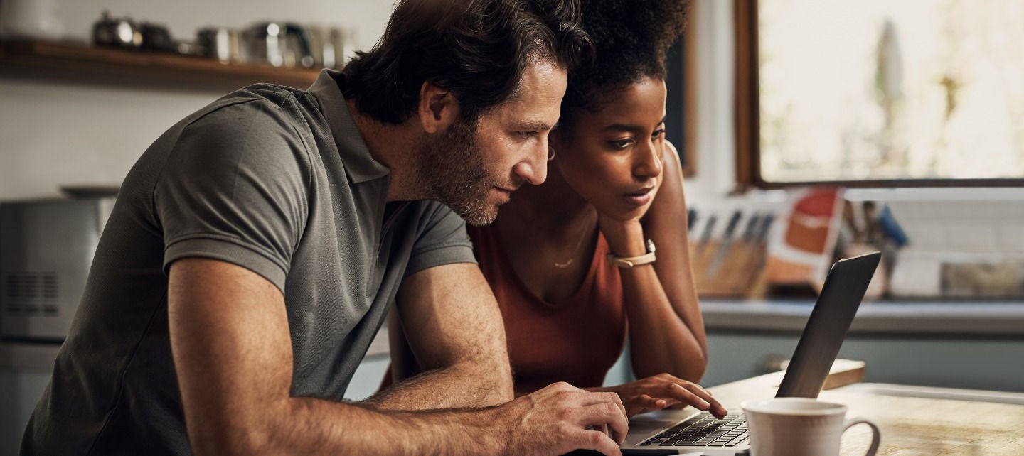 A couple look at their laptop in their kitchen.