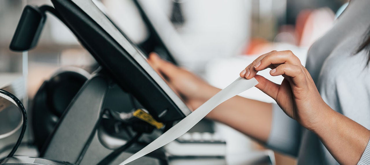 Close-up of cashier’s hands pulling a printed receipt from a POS system