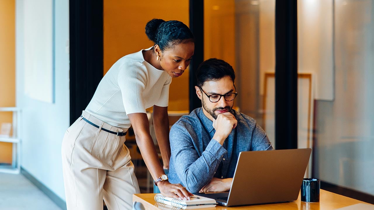 Colleagues focusing on laptop in office.