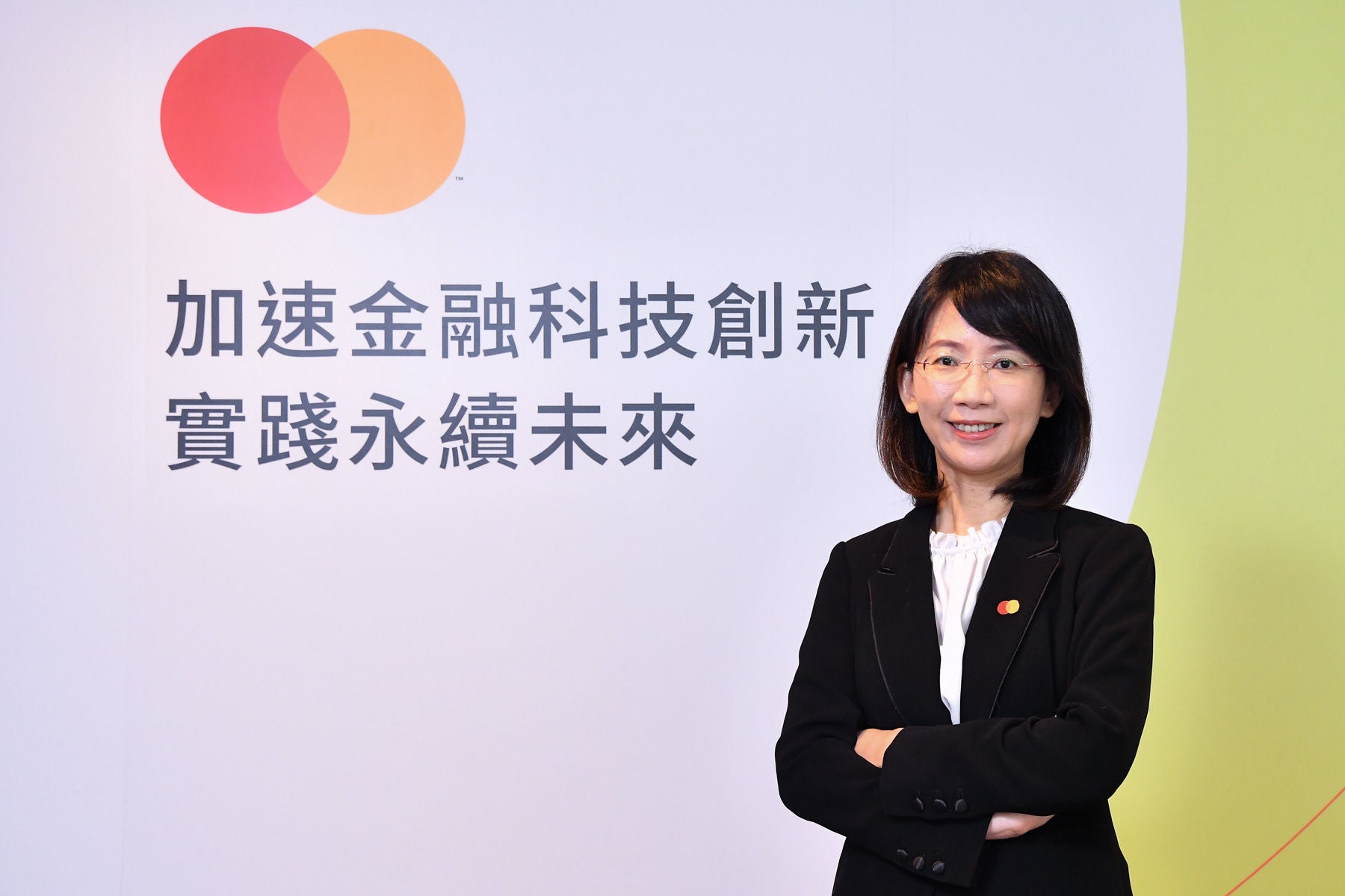 A woman in a black blazer stands with her arms crossed, smiling in front of a white backdrop with Chinese text and a brand logo.
