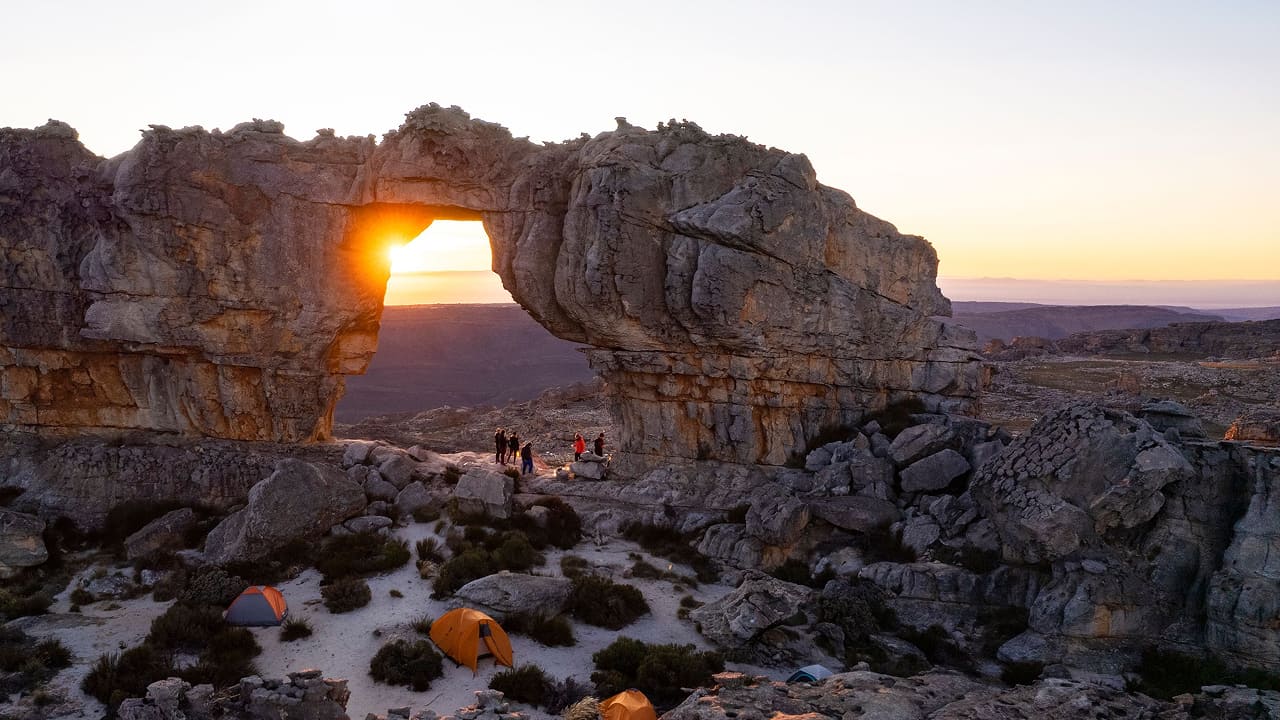 people camping by a rock arch