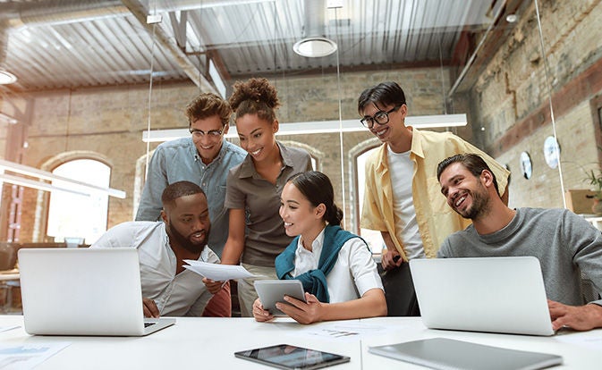 A diverse group of people seated around a table, each using laptops for a collaborative work session.