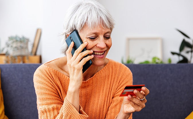Senior woman shopping using credit card talking on phone.