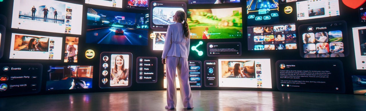Egy nő egy hatalmas digitális kijelzőfal előtt áll, amely közösségi média-, videó- és alkalmazásfelületeket jelenít meg, a digitális tartalom és online élmények sokszínűségét hangsúlyozva.
