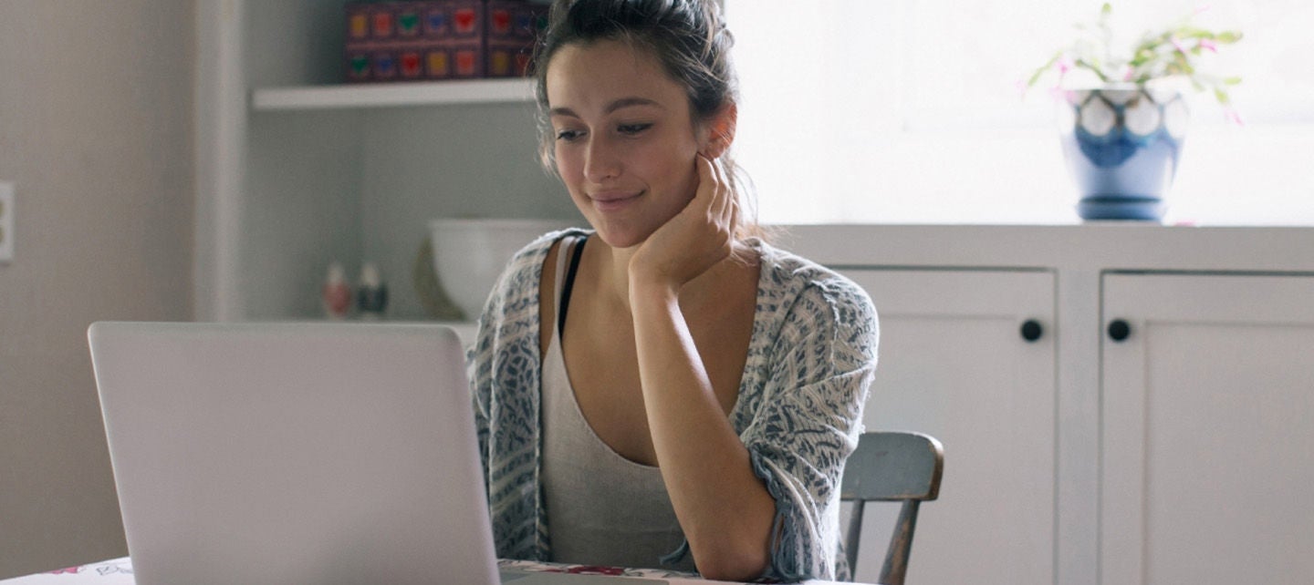 En person som bruker en bærbar datamaskin hjemme, sittende ved et bord.
