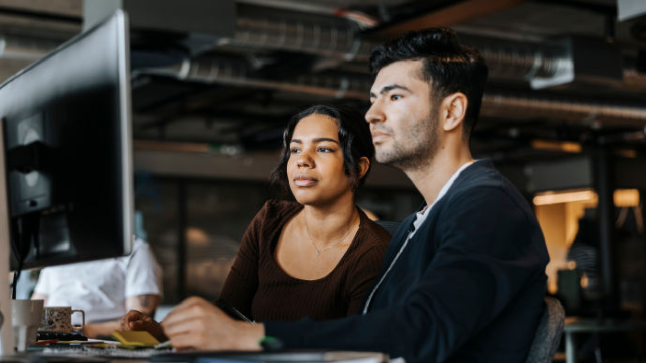 Two people look with concern at a computer in an office. 