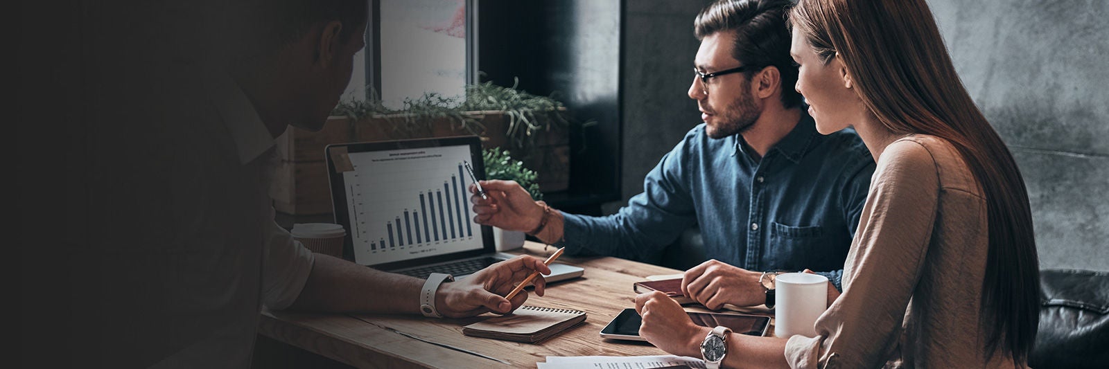 Üzleti megbeszélés: két szakember laptopon megjelenített grafikonokat elemez, jegyzetelnek és egyeztetnek egy asztalnál.