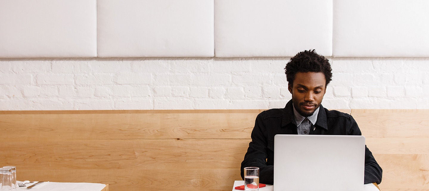 Person sitter alene ved bordet sittende foran laptop i minimalistisk interiørdesign miljø.