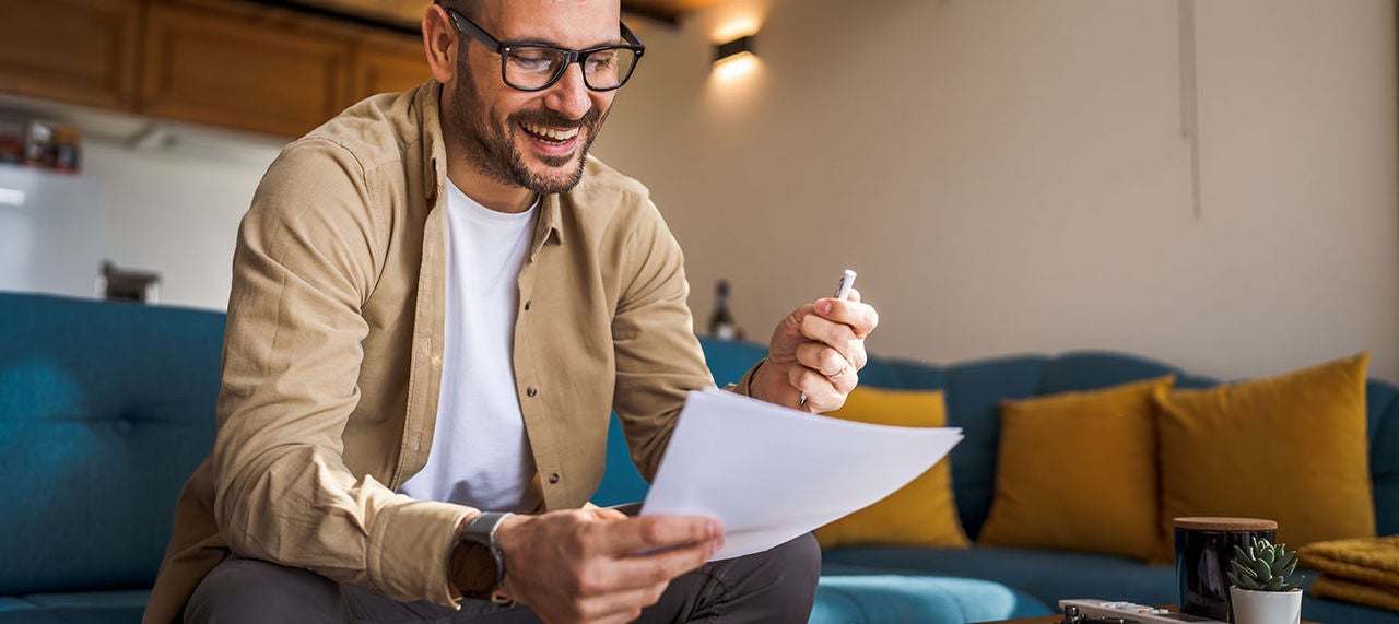 Smiling man sitting on couch at home reviewing financial documents