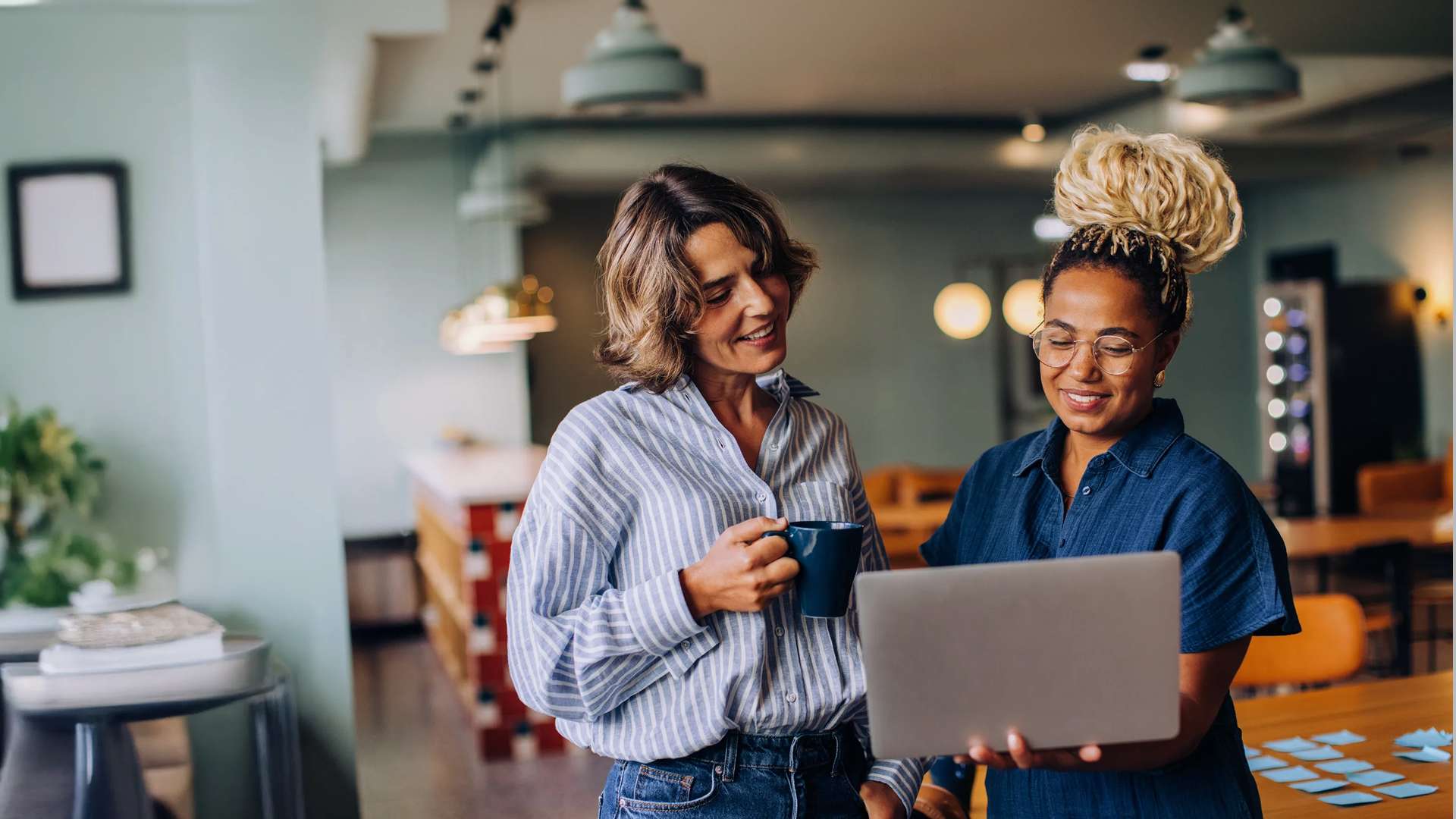 Two women standing in a coffee shop looking at a laptop