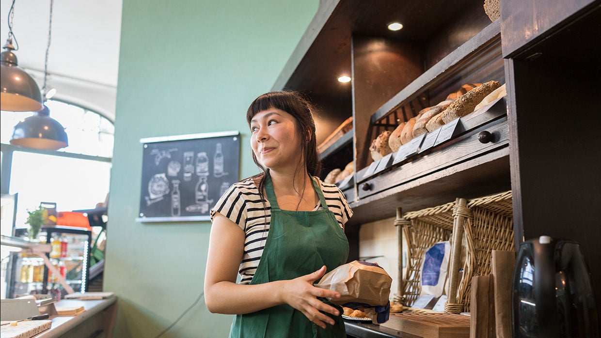 woman in green apron smiling at person in shop