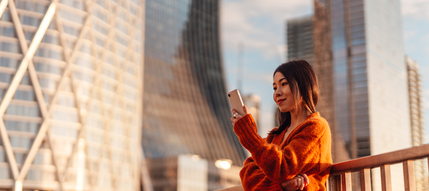 Woman in orange looking at her phone outside