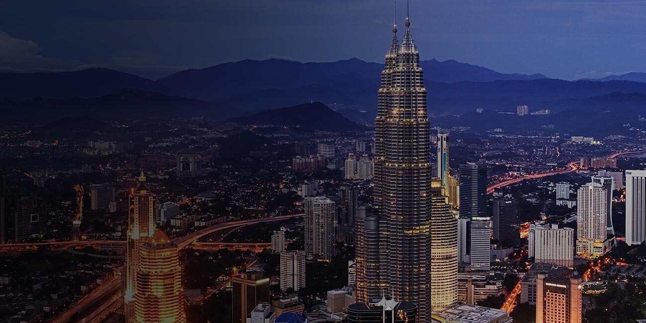 Éjszakai városkép Kuala Lumpurban, kivilágított felhőkarcolókkal és a Petronas-ikertornyokkal a középpontban.