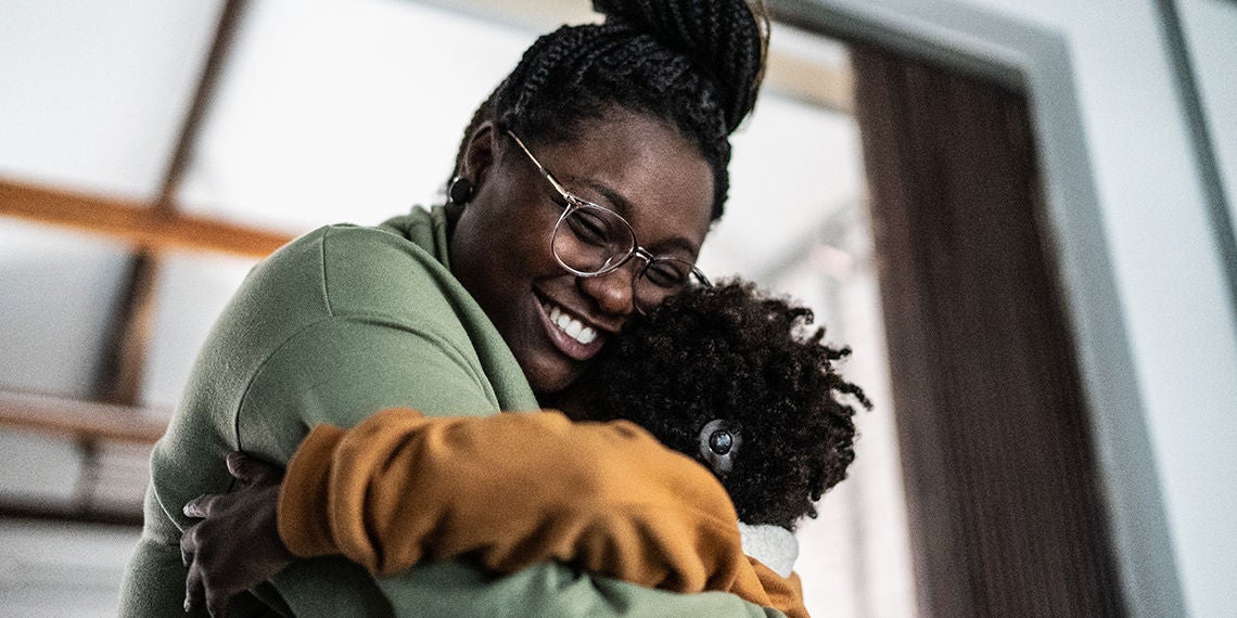 A woman smiles warmly as she hugs a child.