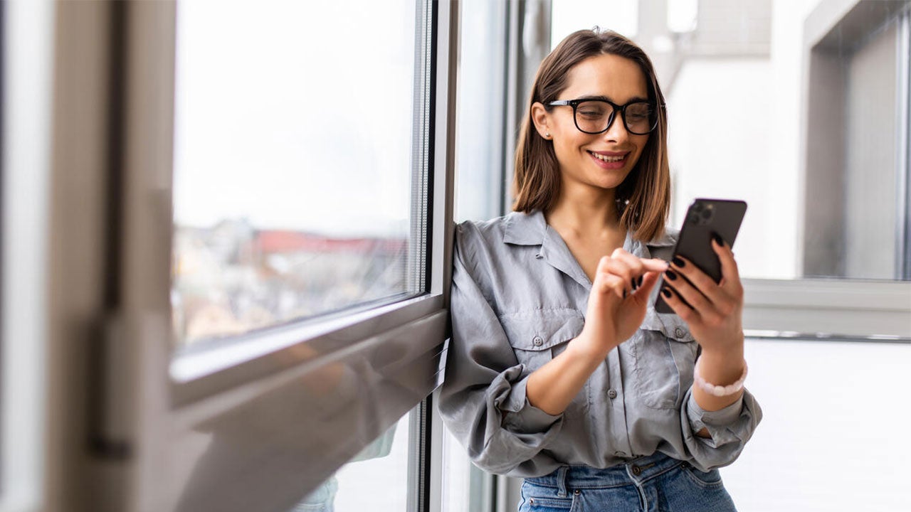 A woman using smart phone near window of the living room.