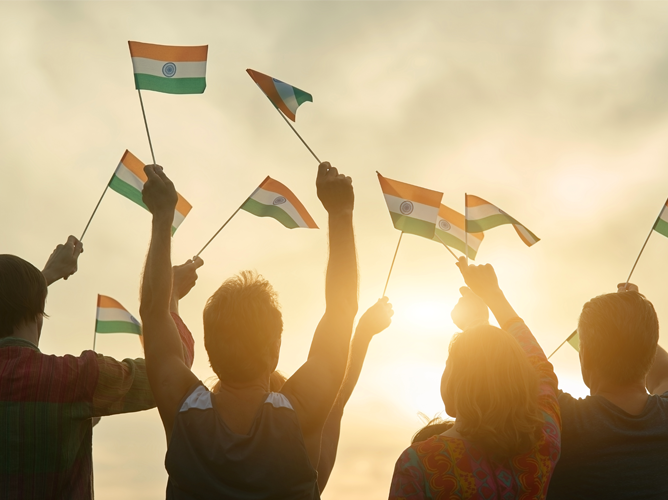 A crowd of celebrating fans waving Indian flags against a sunset, showing national pride and support during the Cricket World Cup.
