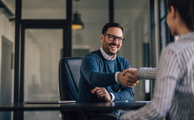 En mann håndhilser på en kollega på et kontor, et symbol på en profesjonell avtale eller samarbeid.