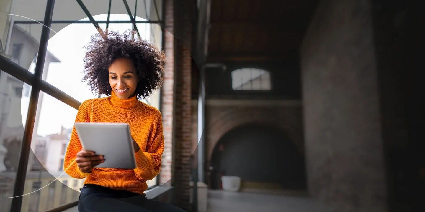 אישה בסוודר כתום מחזיקה טאבלט.