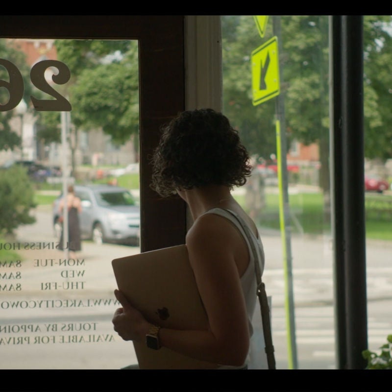 A woman stands inside a business looking out at the street in a small town. 