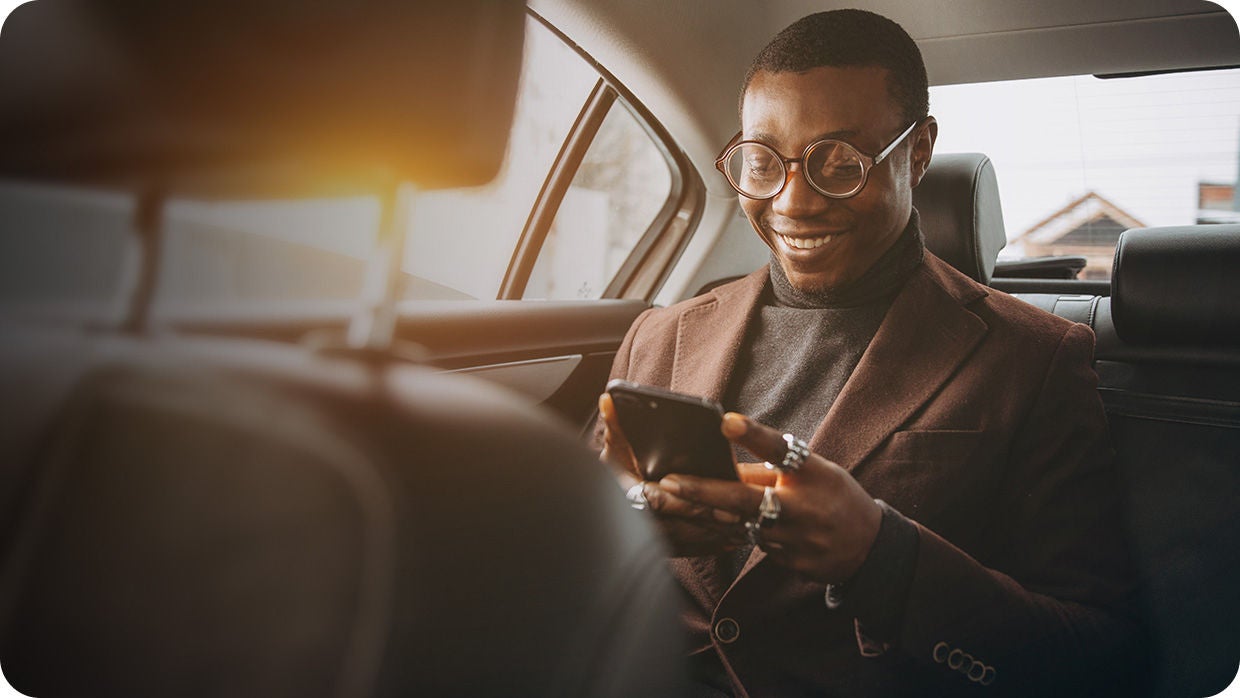 Confident and stylish businessman smiling while checking his phone in the backseat of a car.