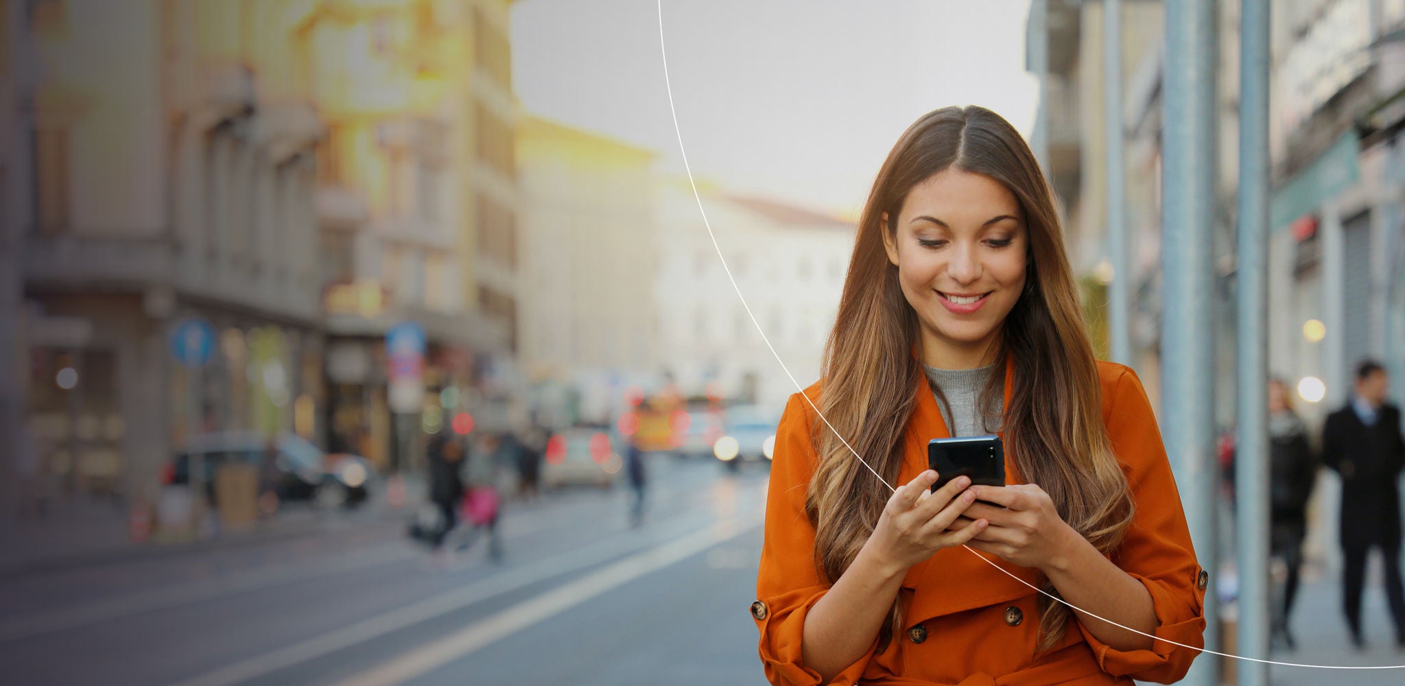 A woman in an orange coat stands on a city street, looking at a smartphone, with a busy urban backdrop.