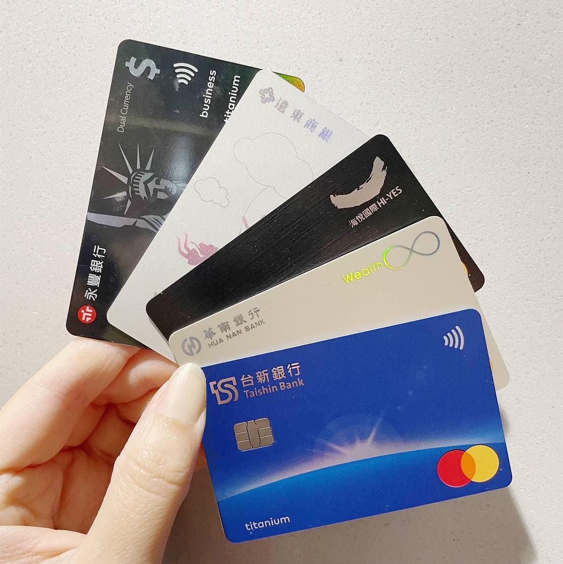 A hand holds five payment cards from different banks fanned out against a white background.