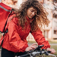 Woman delivery partner riding bike looking at phone.