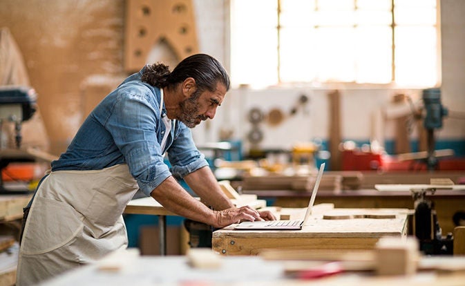 Carpenter in workshop using laptop.