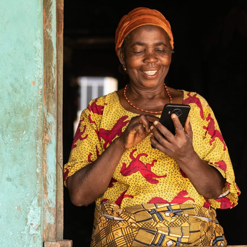 A woman in African print dress standing in a doorway looking at her phone. 