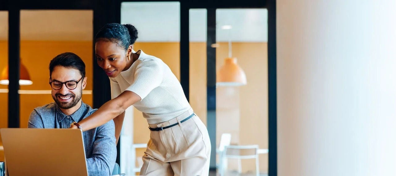 גבר ואישה יושבים ליד שולחן במשרד, עובדים במרץ על מחשב נייד.