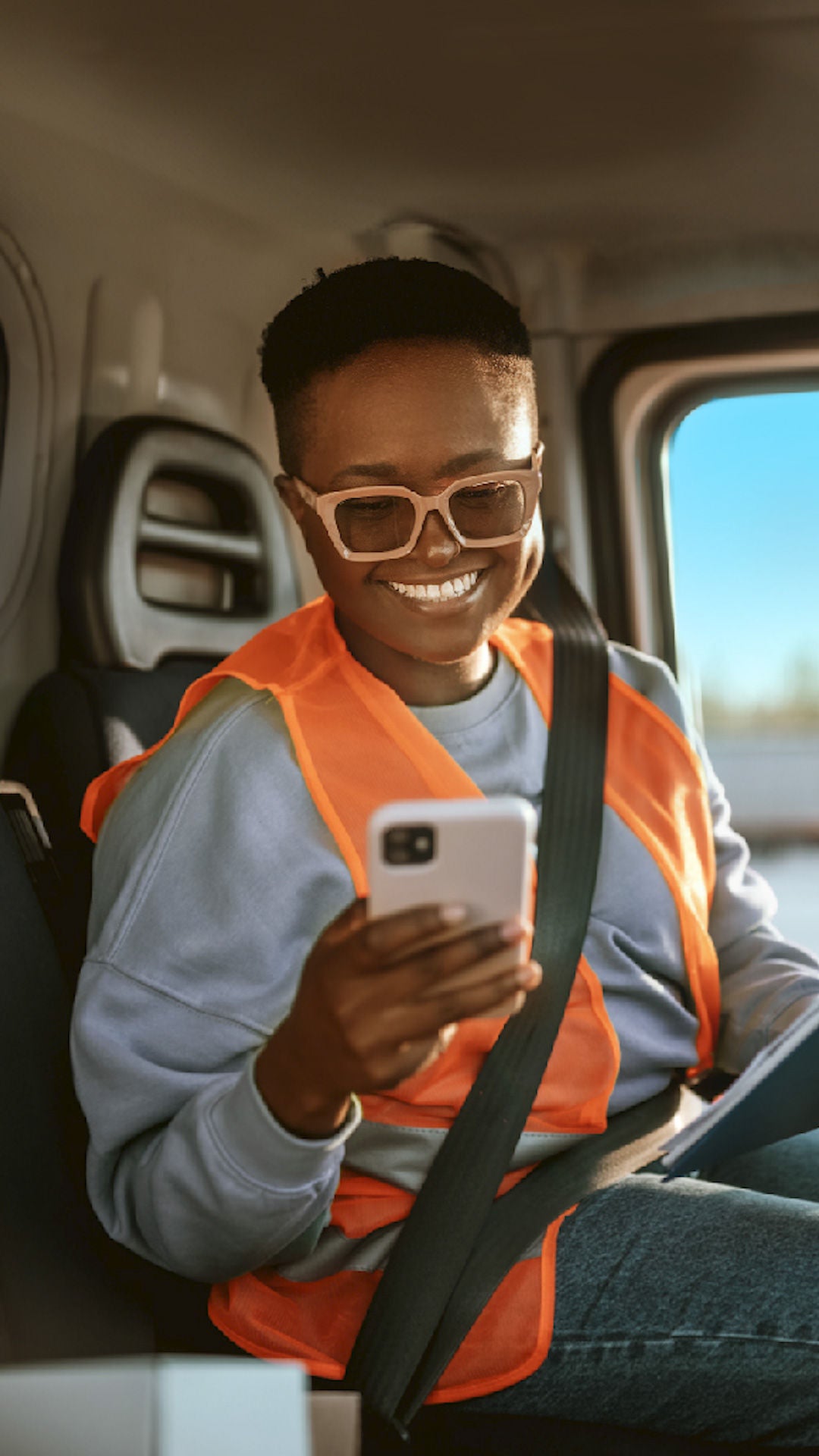 Person wearing a seatbelt in a parked vehicle and looking at a phone.