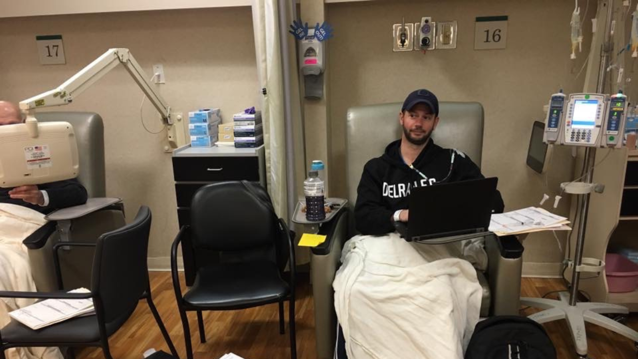 Nick Pifani seated in a chair in front of a laptop ogetting a chemo treatment