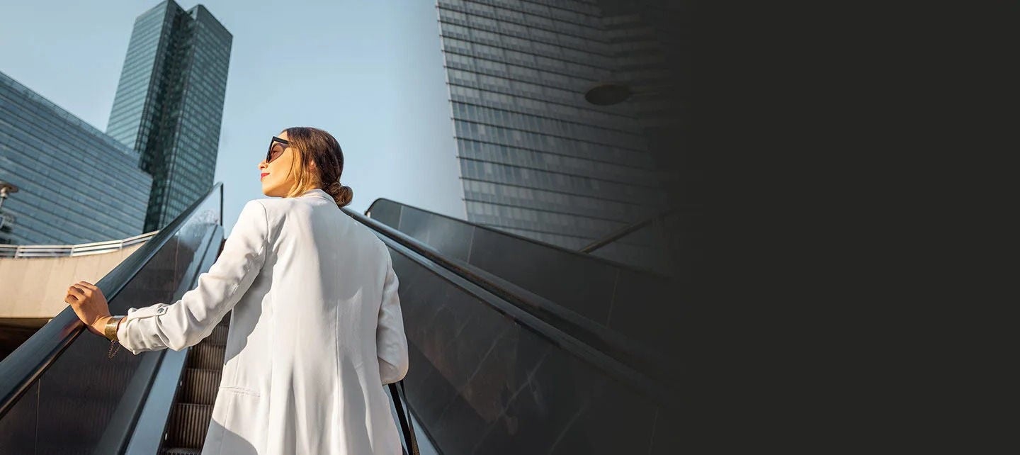 אשת עסקים על מדרגות נעות חיצוניות בין גורדי שחקים.