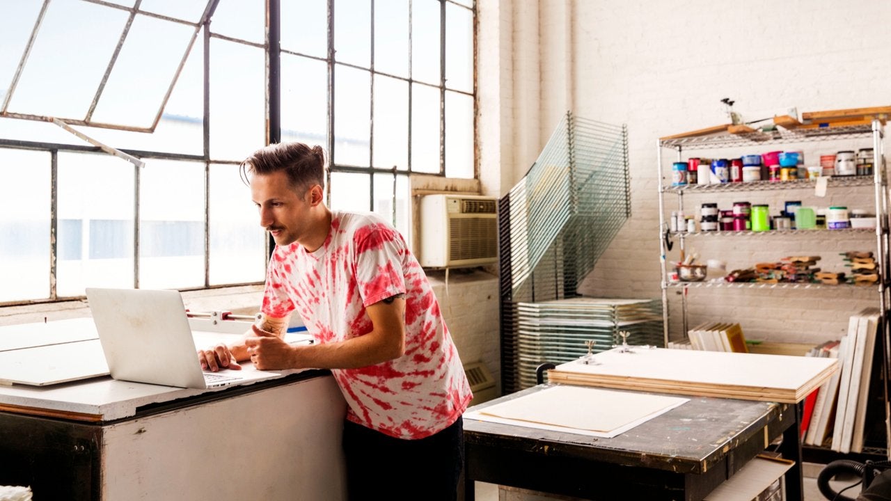 A man in a loft-style studio workshop look at it computer. 