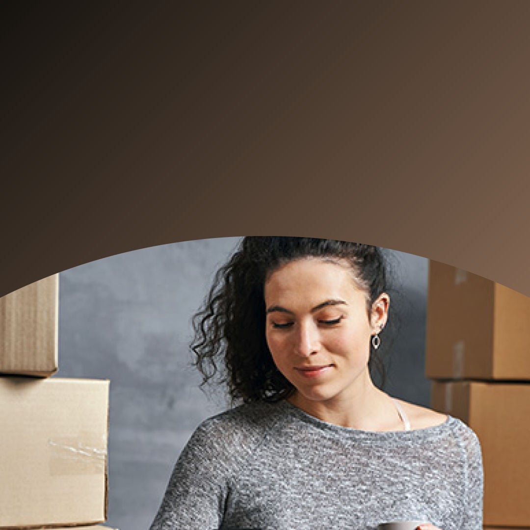 Propietario de una pequeña empresa rodeado de cajas de envío pagando con teléfono. 