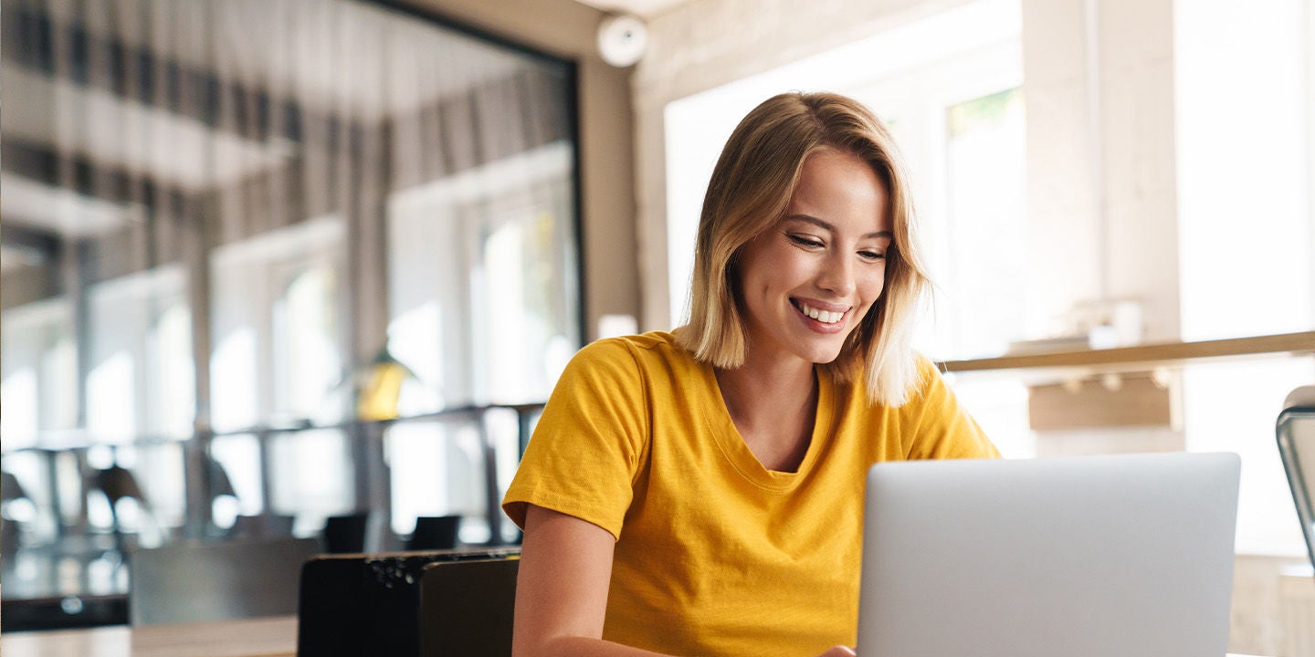 A woman wearing a yellow t-shirt using a laptop