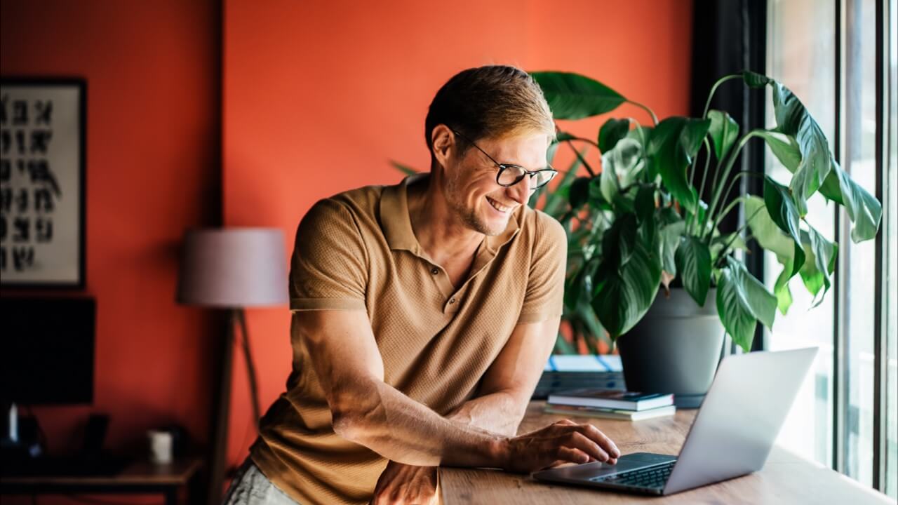 A man is working on laptop orange wall at background