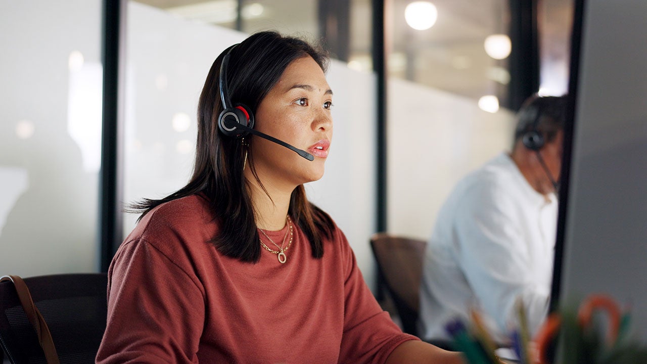 Busy looking woman with headset working on computer in an office.